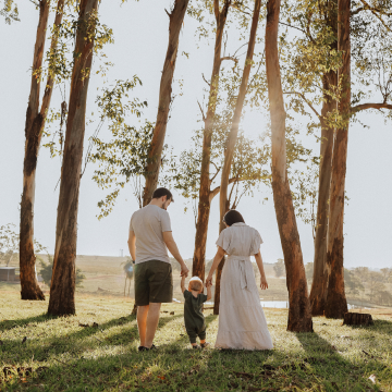 Pai e mãe segurando filho entre as árvores