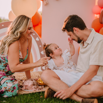Mãe e pai olhando a filha brincar com o bolo de aniversário