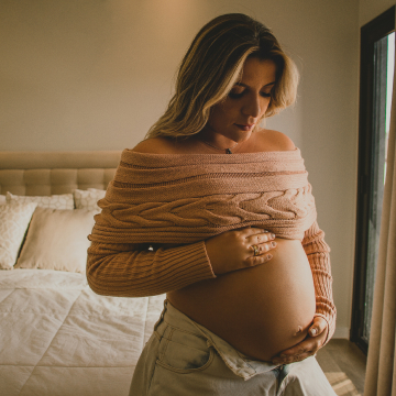 Grávida sentada na cama olhando sua barriga
