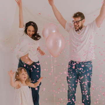 Mãe, pai e filha brincando com balão e pétalas rosas